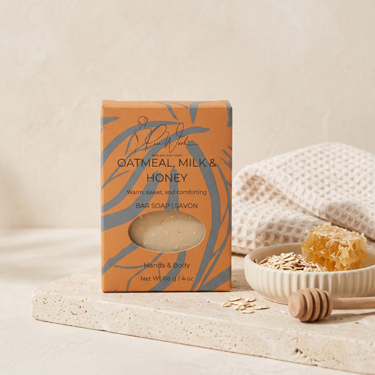 Pure Wash Oatmeal Milk & Honey soap bar in orange packaging with raw honeycomb and oats on a stone tray