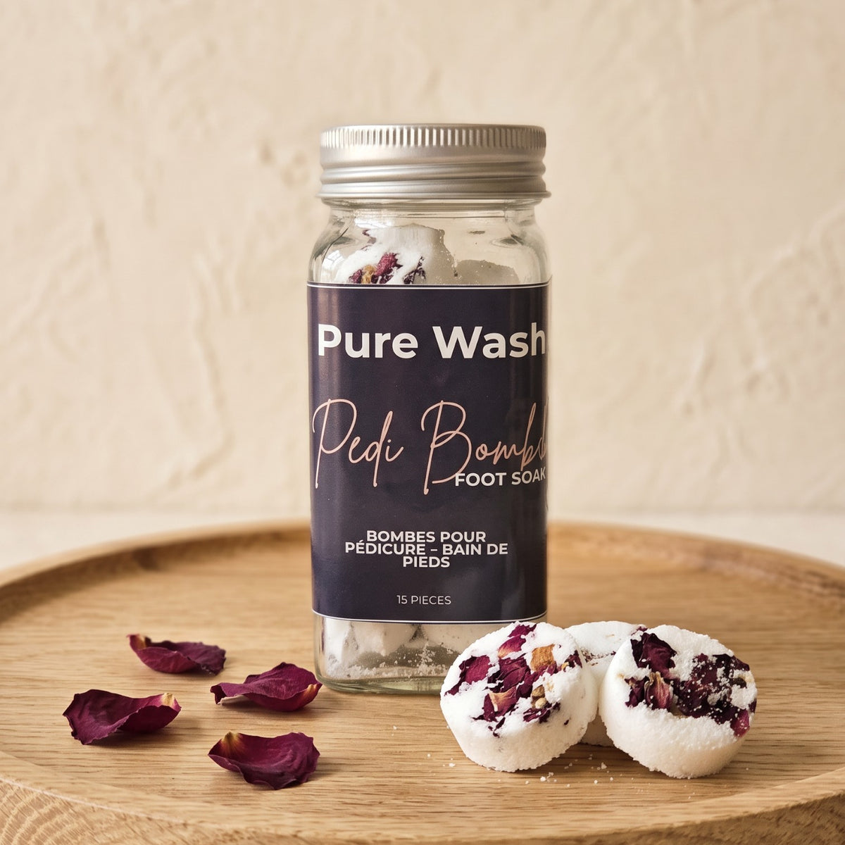 Pure Wash Pedi Bombs in a glass jar with dried rose petals on a wooden tray for a relaxing foot soak experience.
