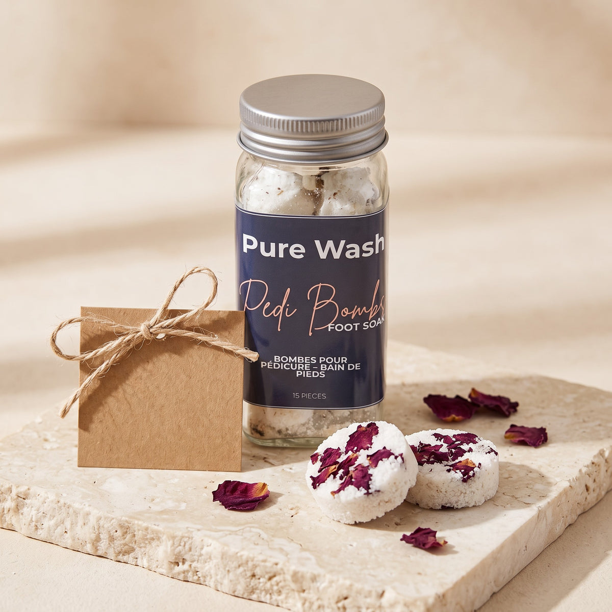 Pure Wash Pedi Bombs in a glass jar with dried rose petals on a stone surface and a blank gift tag