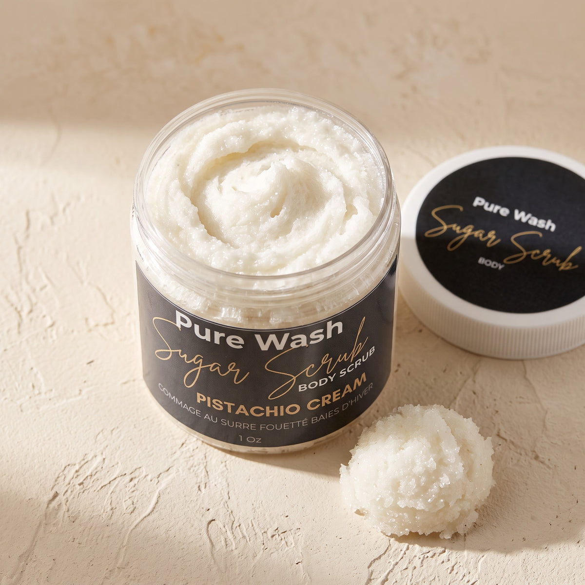 Pure Wash Pistachio Cream body sugar scrub in a clear jar with a black label and a small scoop of scrub on the side.
