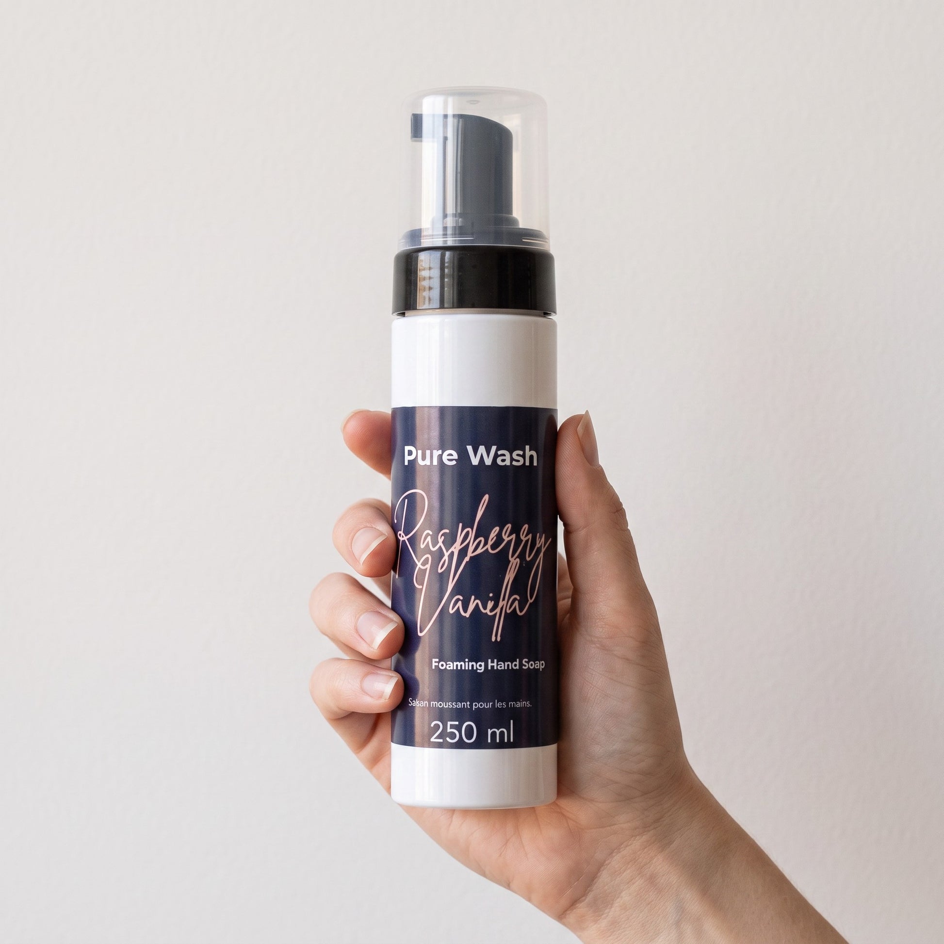 Pure Wash Raspberry Vanilla foaming hand soap in a 250ml pump bottle held in a hand against a neutral background.