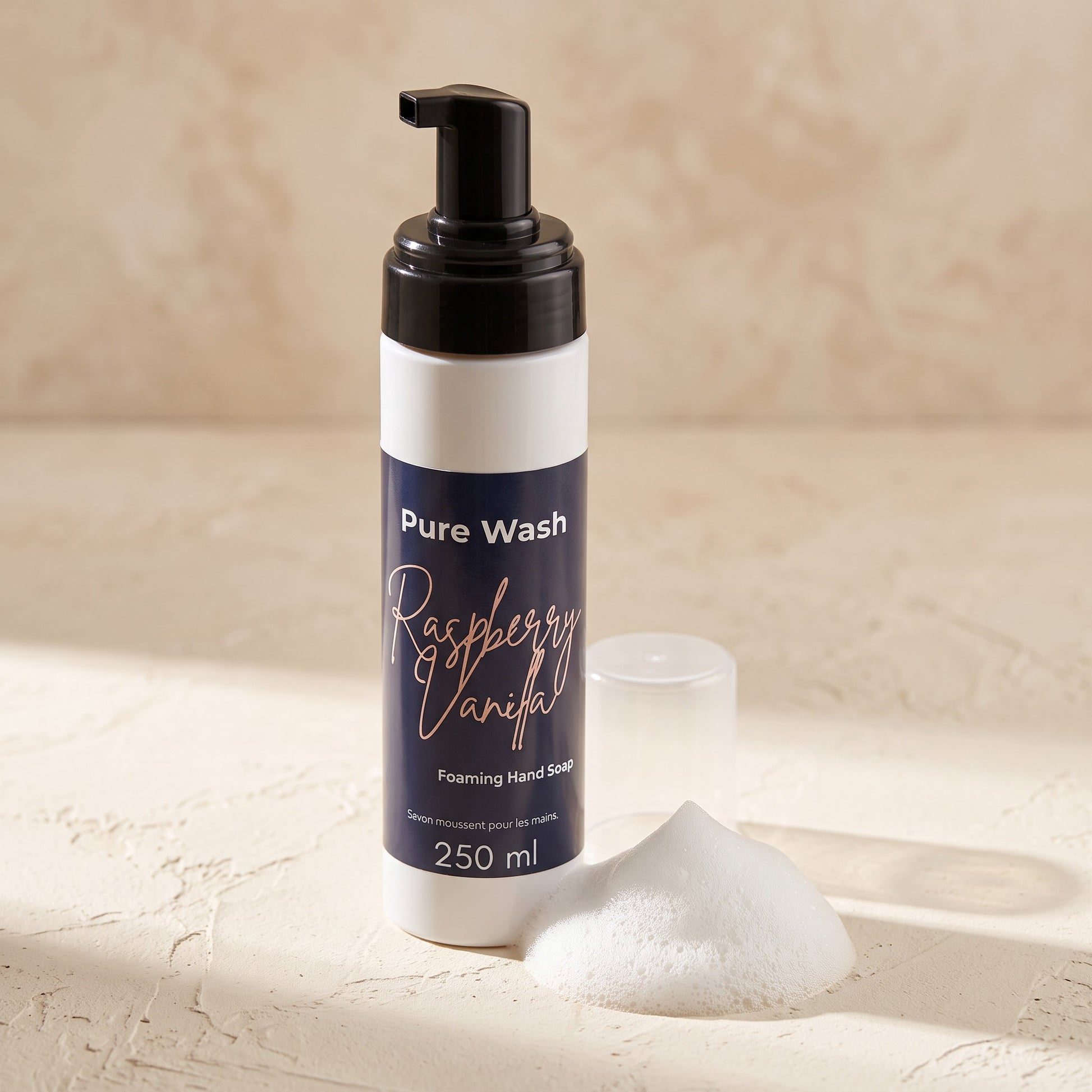 Pure Wash Raspberry Vanilla foaming hand soap bottle with a pump and a dollop of creamy white soap foam on a table.