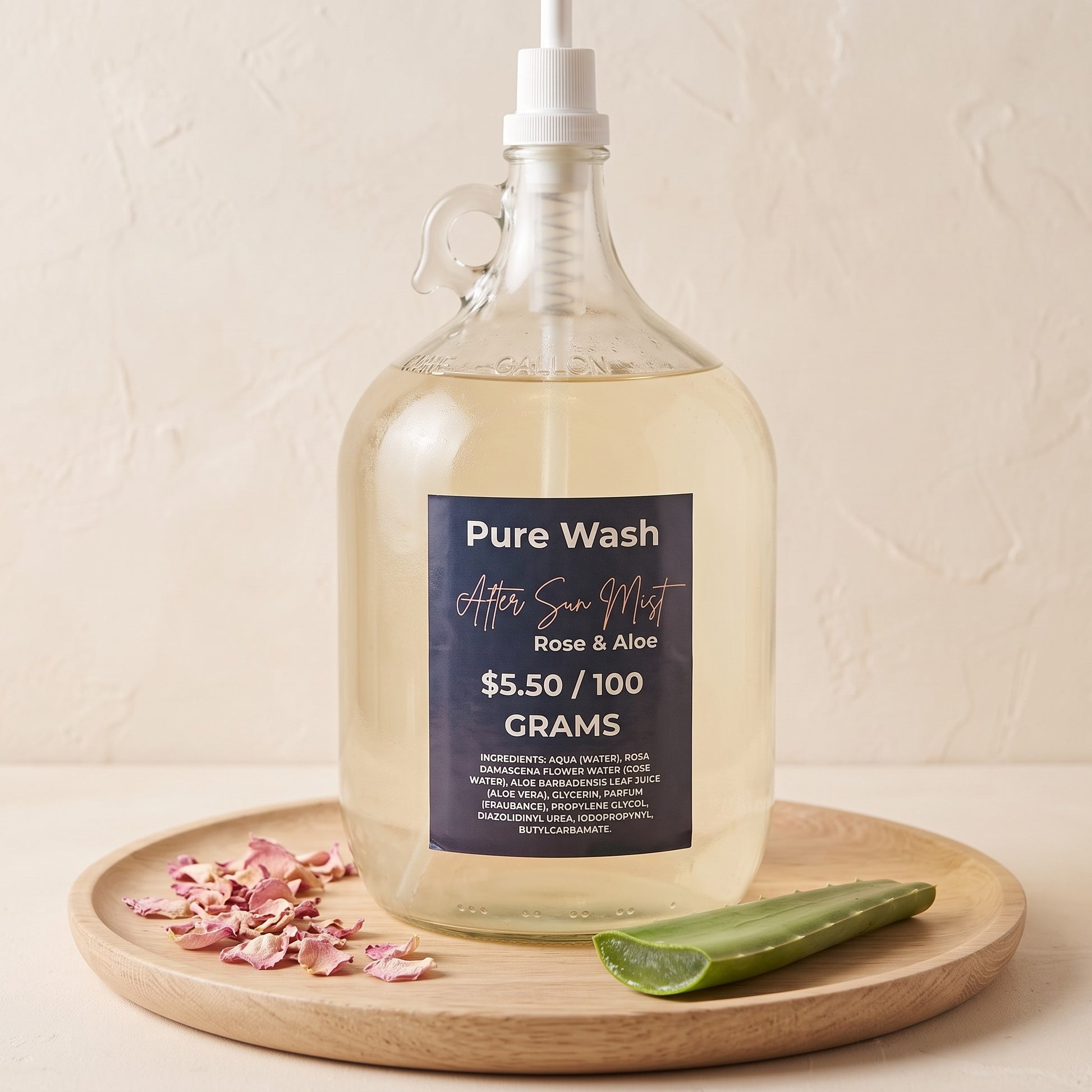 Pure Wash Rose & Aloe after-sun hydrating mist in a large glass refill jug with dried rose petals and aloe vera leaf.