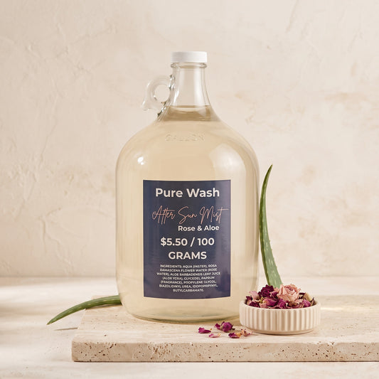 Pure Wash Rose & Aloe after-sun hydrating mist in a large glass refill jug with aloe vera and dried rose petals.
