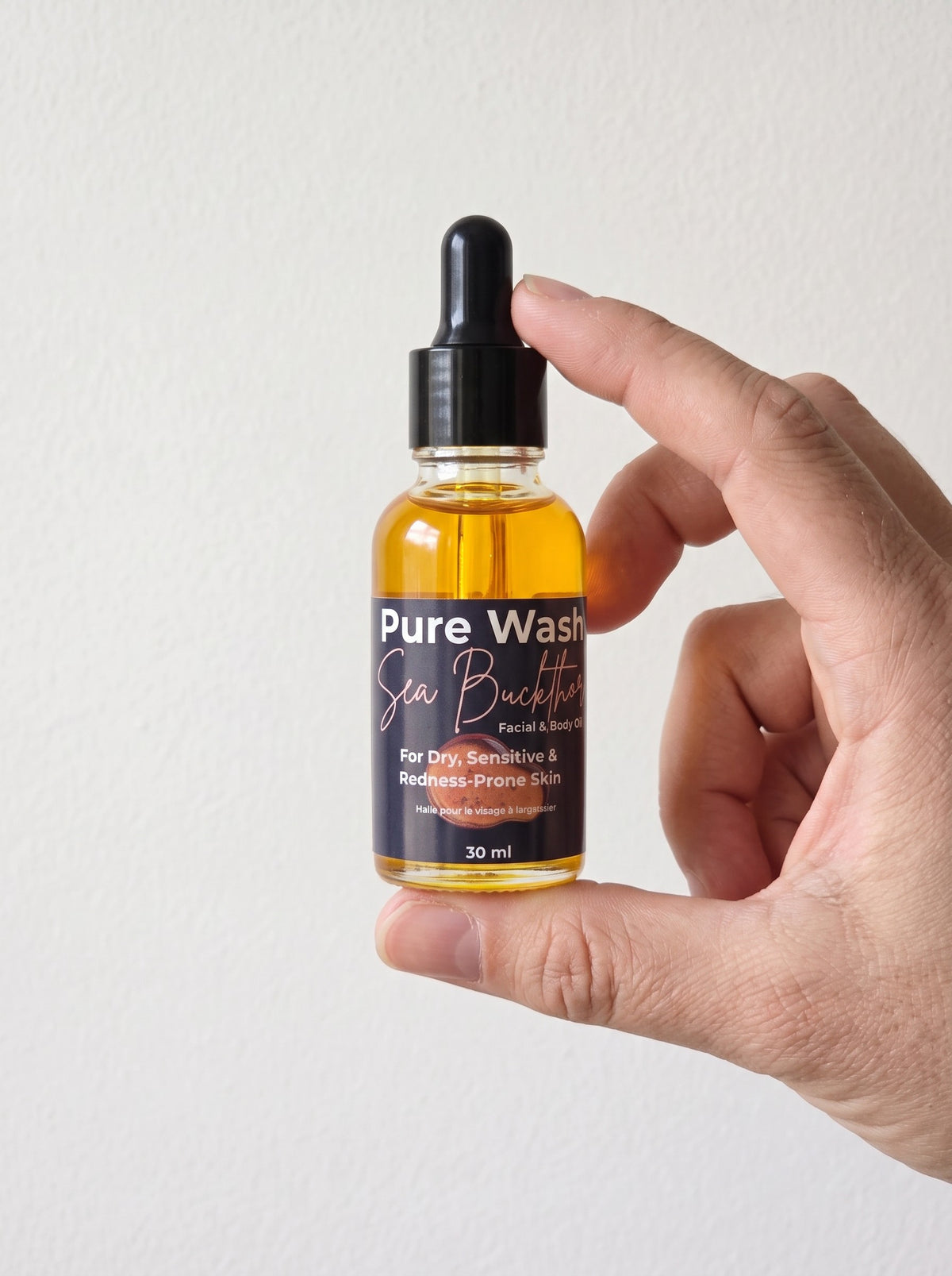 Pure Wash Sea Buckthorn facial oil in a 30ml glass dropper bottle held by a hand against a white background.