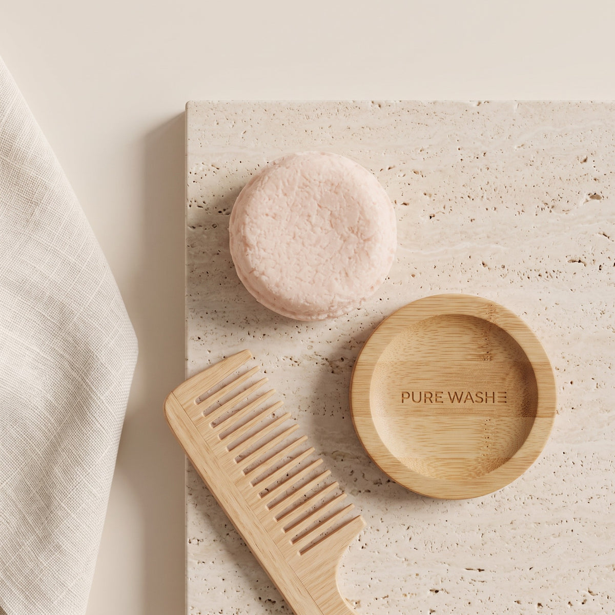 Pure Wash solid shampoo bar in light pink with a wooden comb and soap dish on a textured stone surface