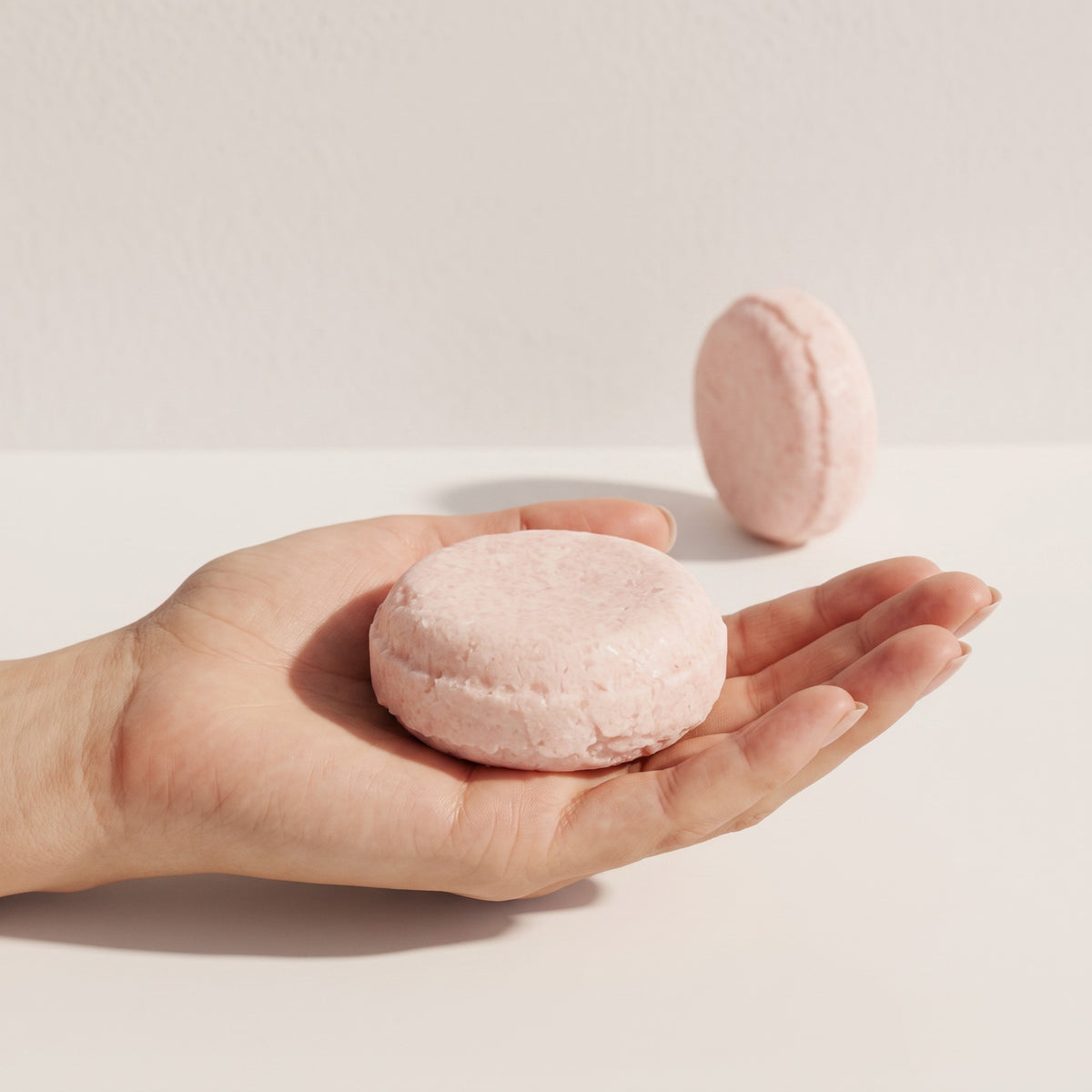 Pure Wash solid shampoo bar in a soft pink shade held in a palm, featuring a rich botanical formula for hair care.