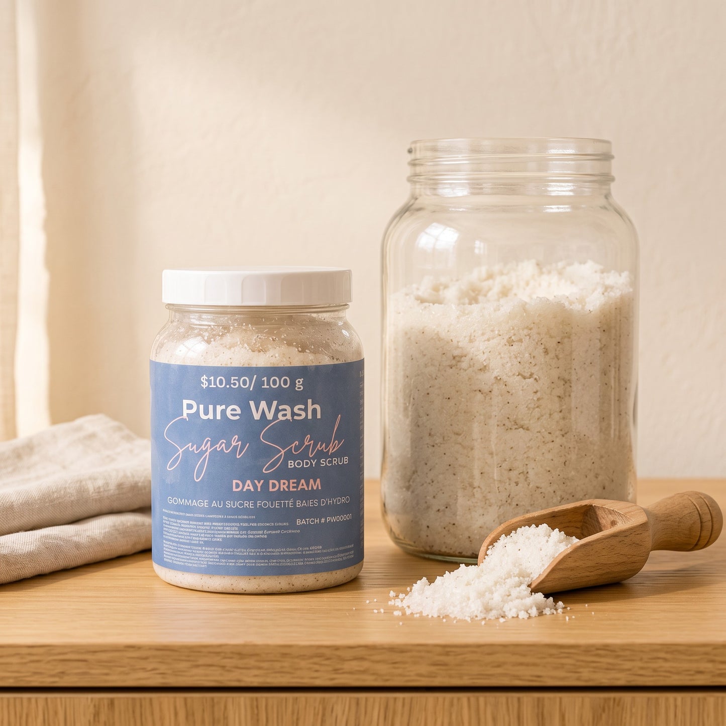 Pure Wash Day Dream sugar body scrub in a jar next to a refill container and a wooden scoop on a wooden table.