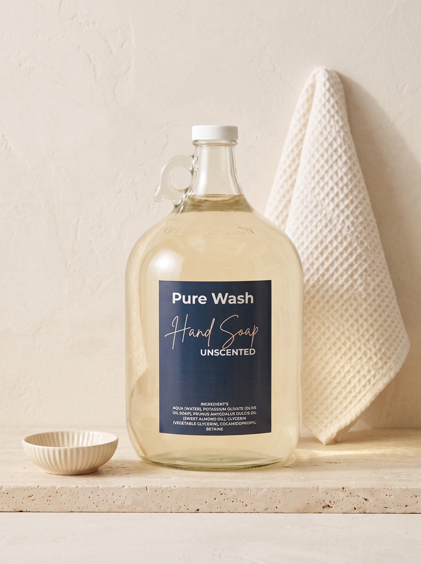 Pure Wash unscented plant-based liquid hand soap in a large glass refill jug on a stone surface with a waffle towel.