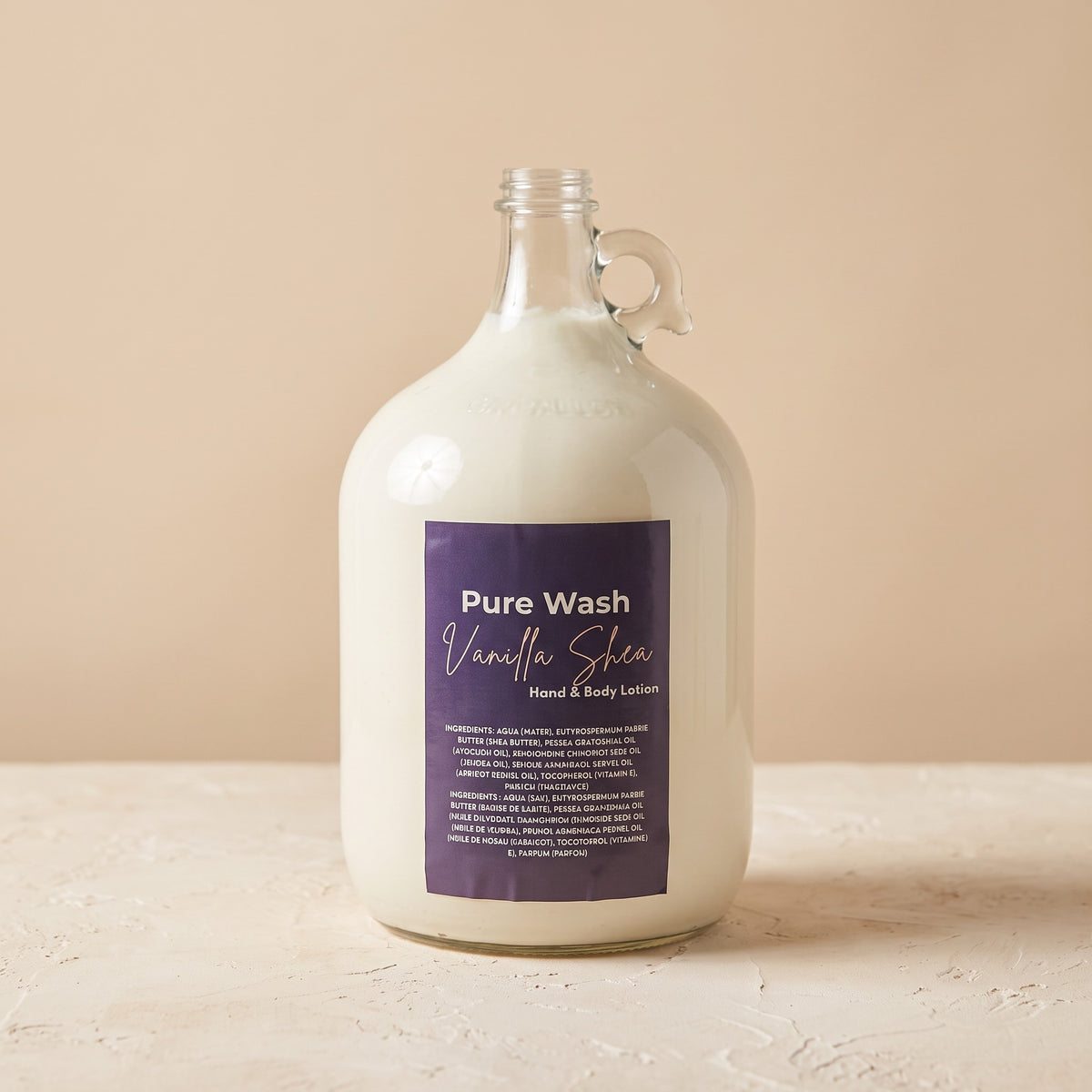 Pure Wash vanilla shea hand and body lotion in a large glass refill jug with a purple label on a beige surface.