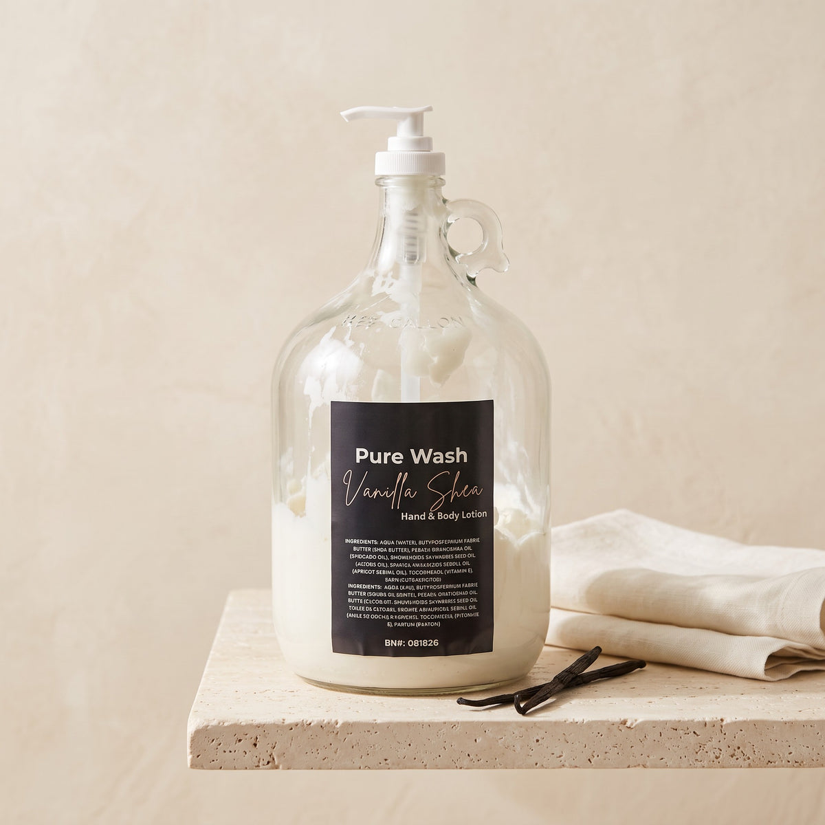 Pure Wash vanilla shea body lotion in a large glass refill jug with a pump dispenser on a stone surface.