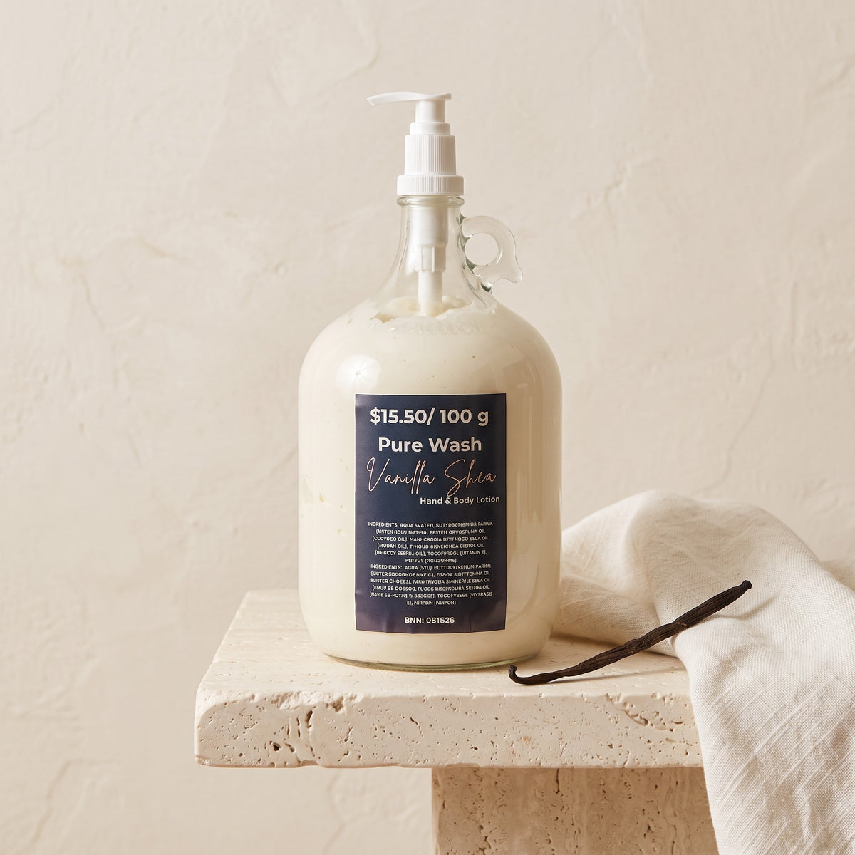 Pure Wash Vanilla Shea body lotion in a large glass refill jug with a pump dispenser on a textured stone pedestal.