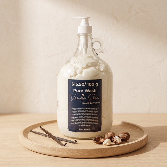 Pure Wash Vanilla Shea body lotion in a large glass refill jug with pump, displayed on a wooden tray with shea nuts.
