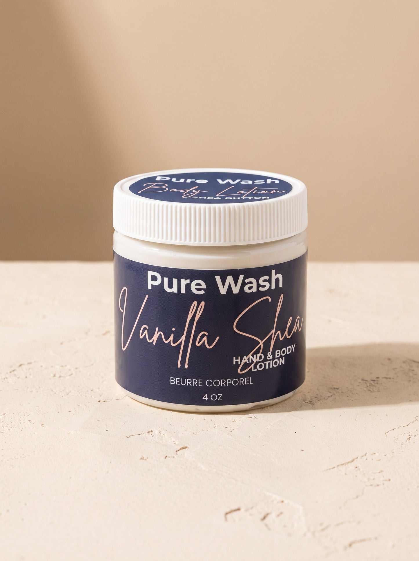 Pure Wash Vanilla Shea hand and body lotion in a 4 oz white jar on a textured beige surface.