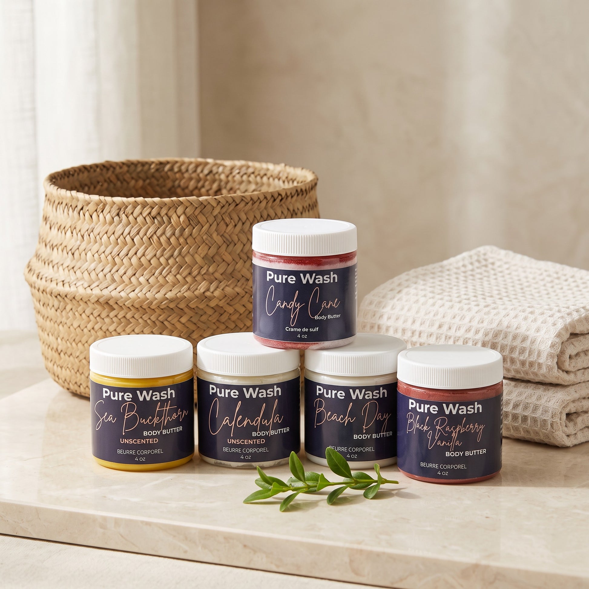 Pure Wash whipped body butter jars in various scents displayed on a marble surface with a woven basket and towel.