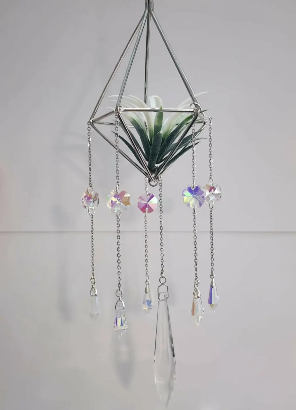 A geometric silver metal pyramid suncatcher with an air plant and colorful crystal beads for canadian made skincare decor
