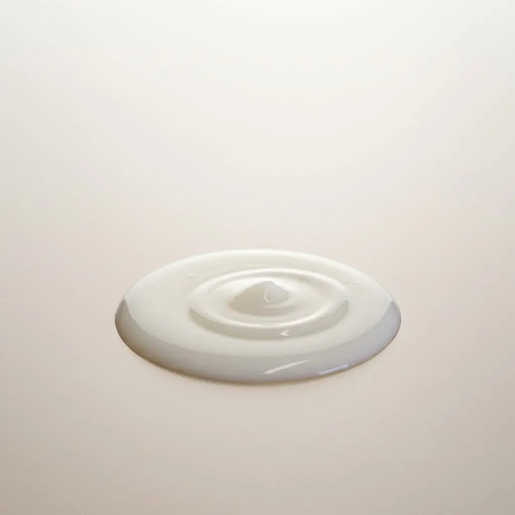 A smooth creamy white serum with seed oil forming a ripple on a light surface for refill station use