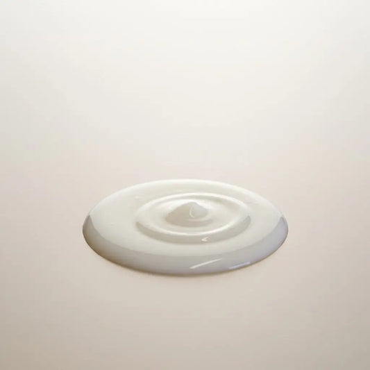 A smooth creamy white serum with seed oil forming a ripple on a light surface for refill station use