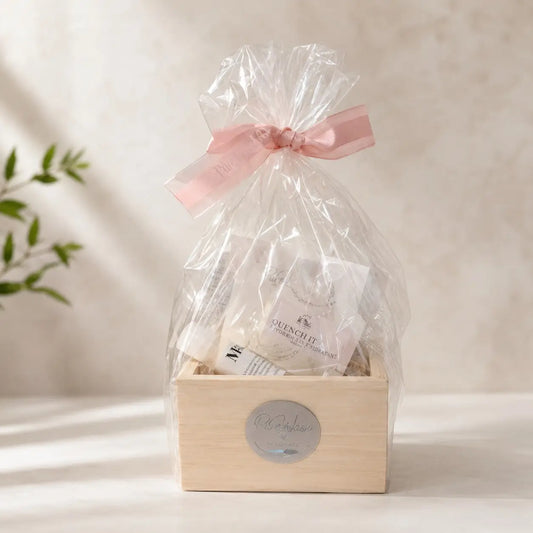 A delicate pink satin ribbon bow on clear cellophane wrapping a wooden natural skincare gift box with exfoliation bar