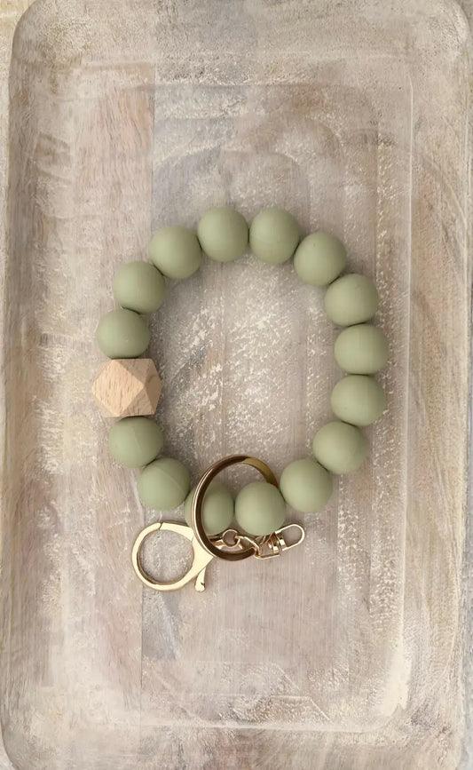 A sage green silicone beaded wristlet with wooden hexagon accent and gold-tone clasp in single colour design