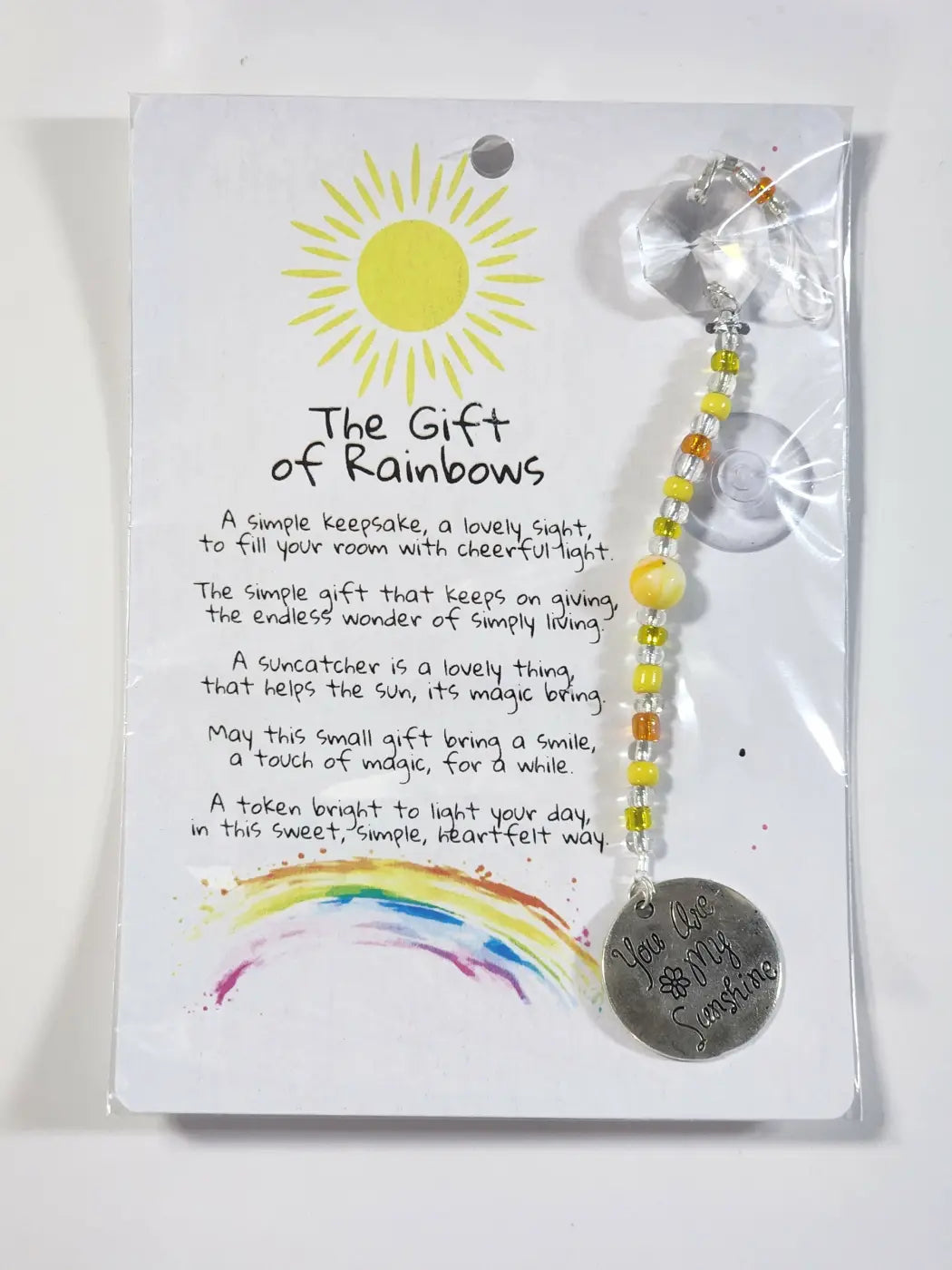 A silver circular small suncatcher pendant with engraved text hangs from yellow and orange beads for window display natural skincare canada