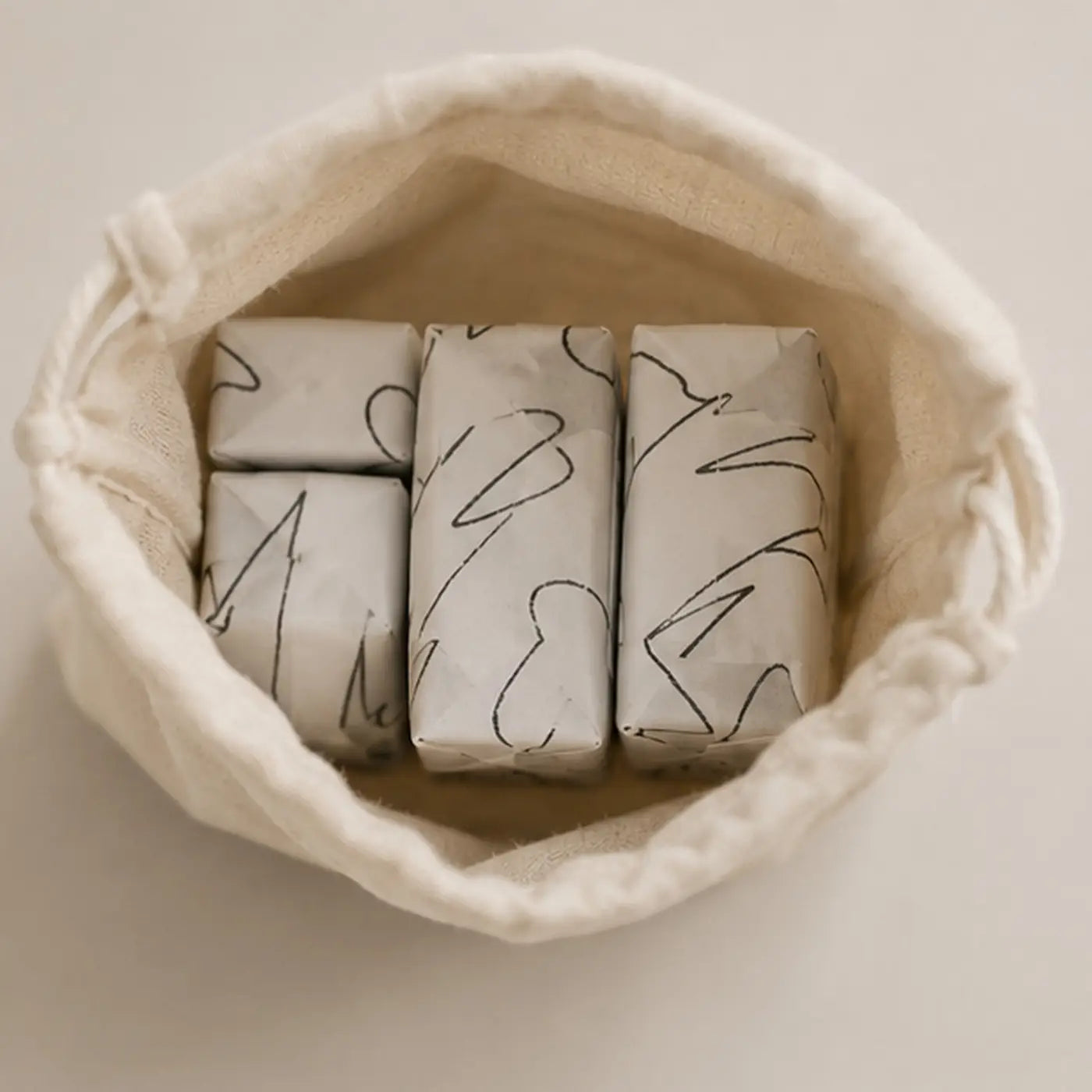 A cream cotton canvas drawstring bag containing four botanical soap bars wrapped in white paper with black line art