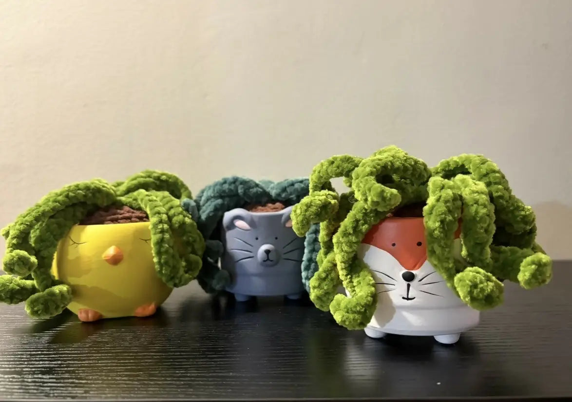Three whimsical ceramic animal pots shaped like yellow chick gray cat and white fox holding spider plants
