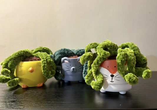 Crocheted spider plants in ceramic animal pots shaped like a yellow chick, a grey cat and a white fox