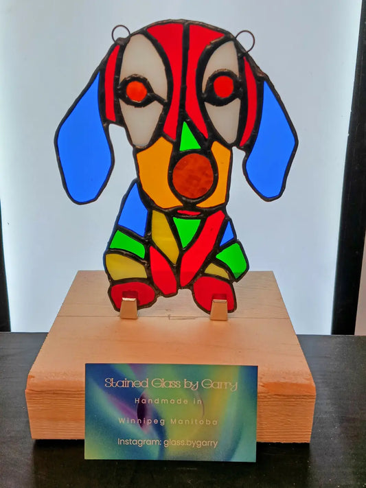A colorful stained glass floppy-eared dachshund sculpture with red blue green and orange segments on a wooden base