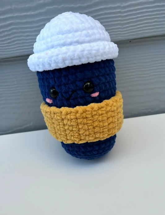 A navy blue crocheted take out coffee with sleeve amigurumi featuring a white lid and yellow scarf for canadian made skincare