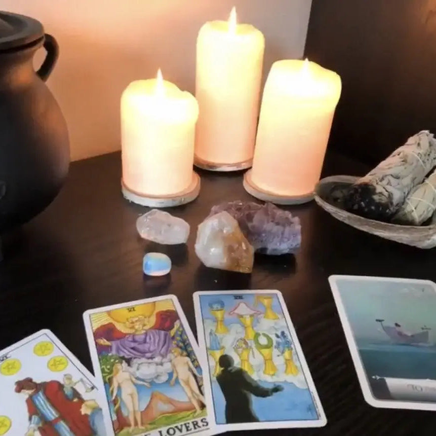Three lit creamy-white pillar candles with smooth rounded tops on dark surface for tarot reading use in canadian made skincare context