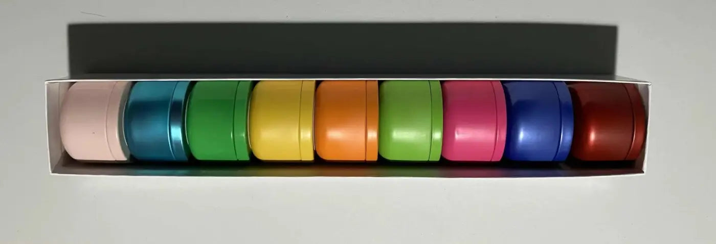 Rainbow-colored metallic cylindrical containers of pure wash hand-poured candles in the fruity candle collection with juicy scents