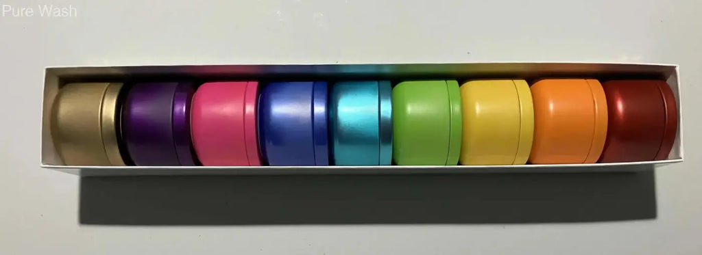 Rainbow candle collection featuring metallic cylindrical tins in various colors including a blue tin candle in a white box labeled pure wash