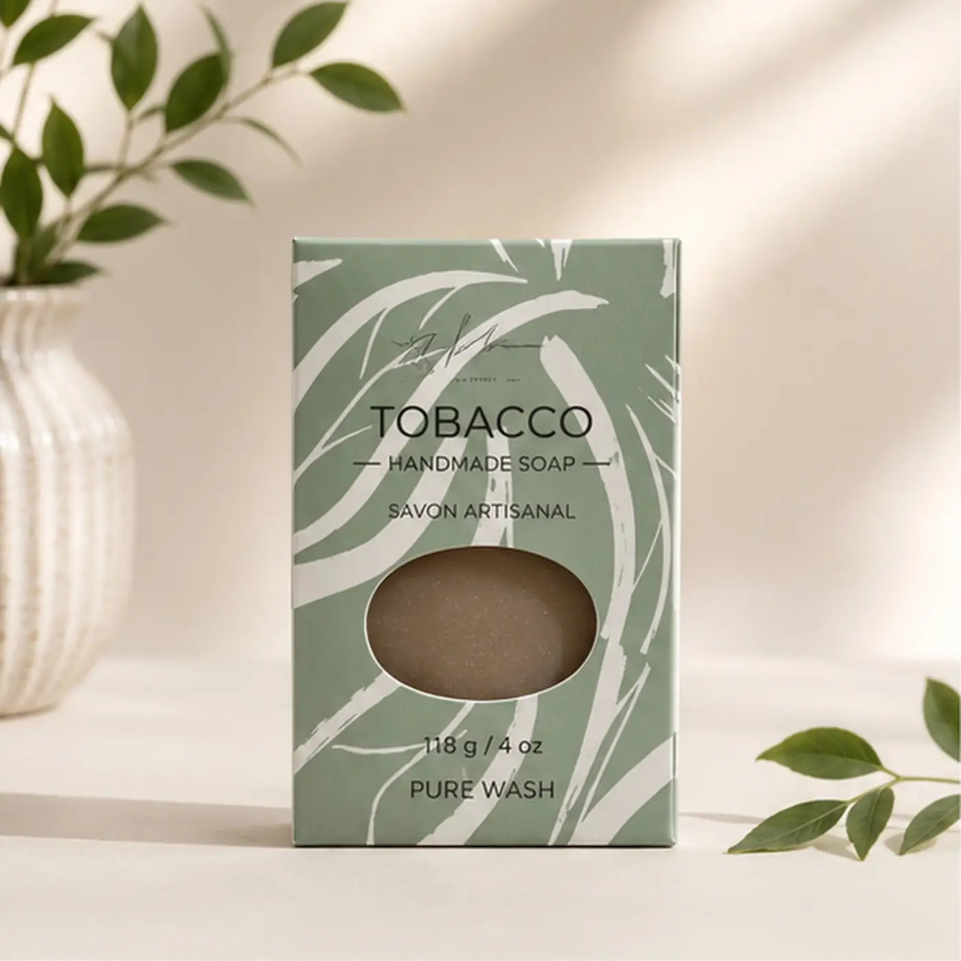 A matte sage green tobacco leaf soap box with white brushstrokes reveals a brown tobacco-scented handcrafted soap bar