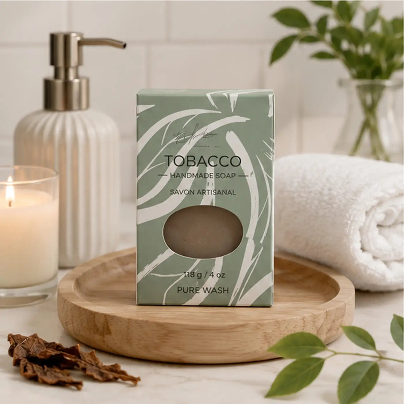 A rectangular box of tobacco leaf soap featuring a sage green leaf design and an oval window showing the brown handcrafted skincare bar with palm oil