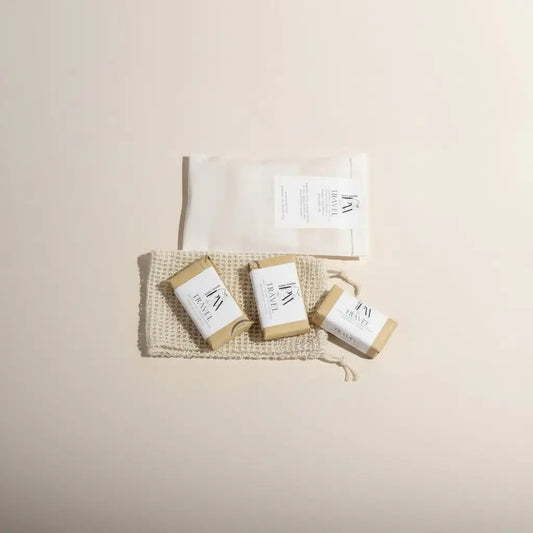 Three rectangular travel mini soap bars wrapped in beige paper with white label featuring black text and logo