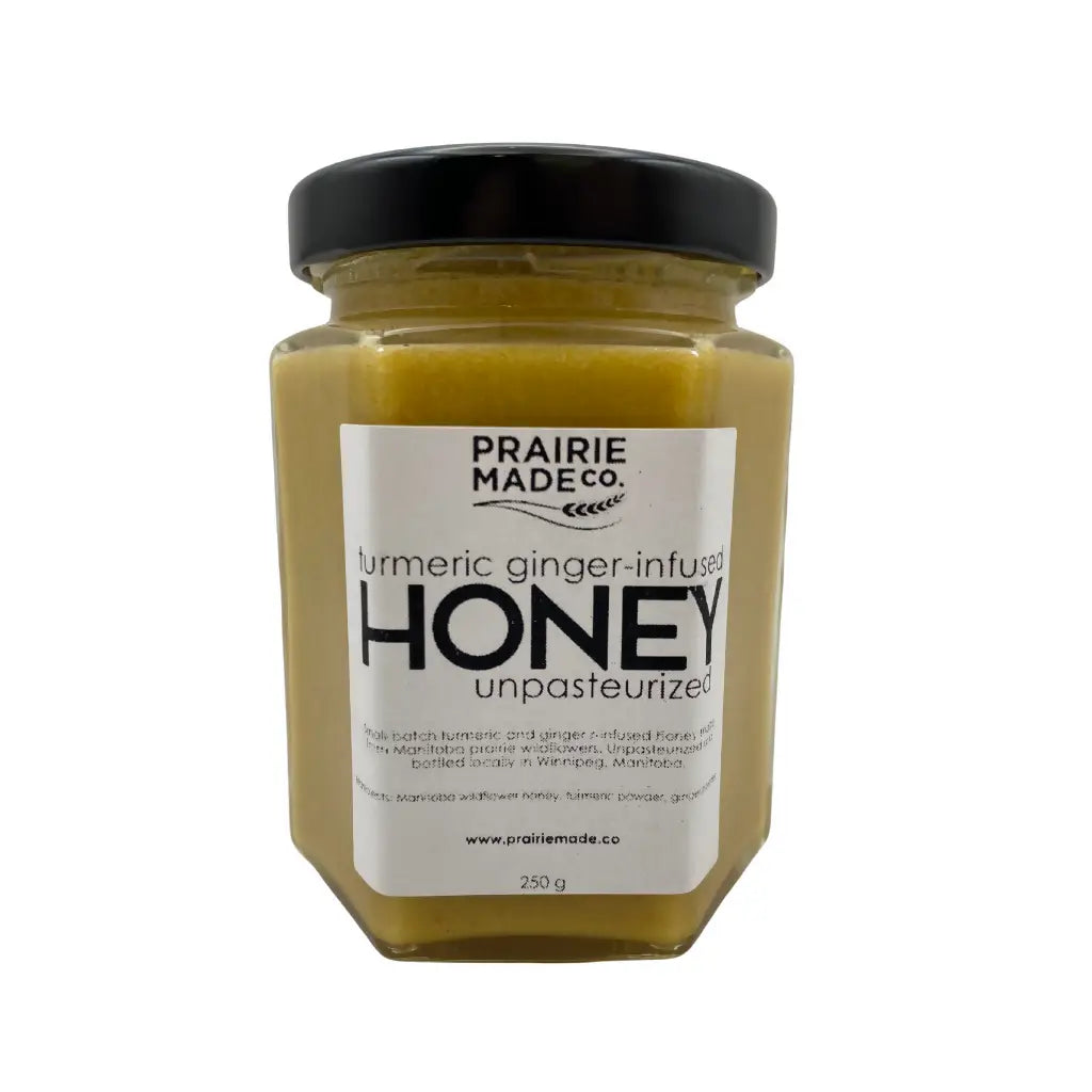 A hexagonal glass jar of prairie made co turmeric ginger infused honey with bold small batch blend and manitoba wildflower honey