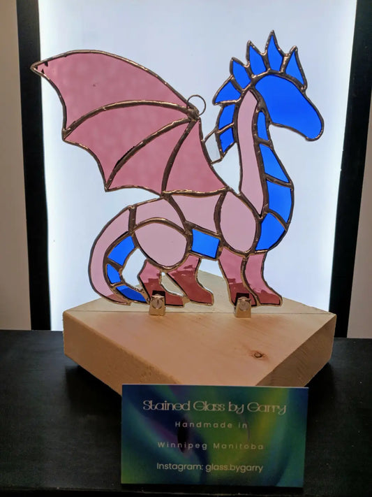 Whimsical dragon handmade stained glass sculpture with pink and blue colors and metallic outlines on a wooden base