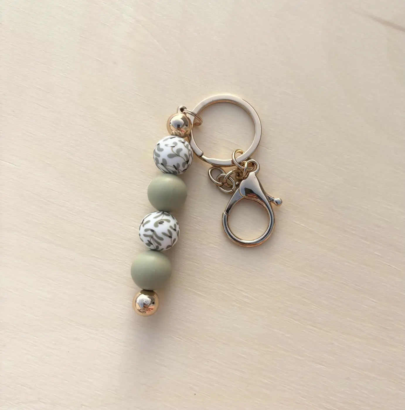 A winter floral silicone bead keychain with matte sage green and white leopard-print beads and silver metal accents