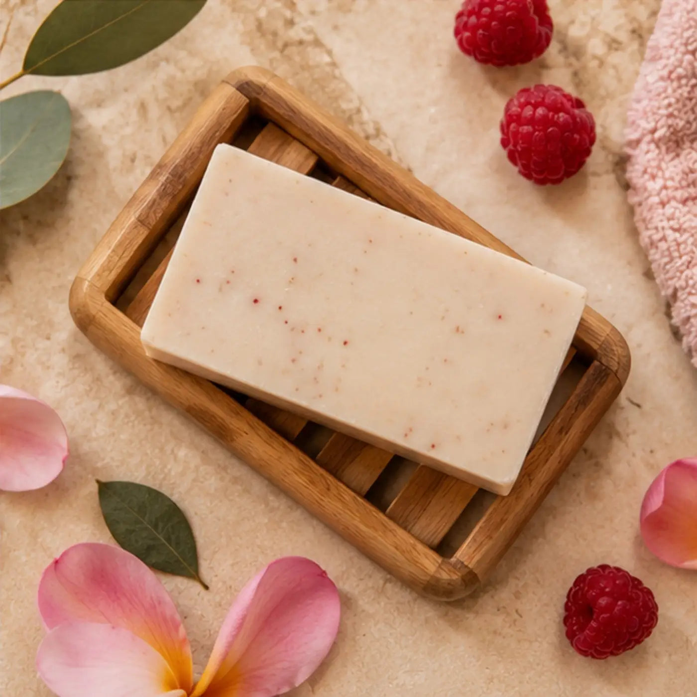 A rectangular off-white handmade winterberry soap bar with red speckles rests in a light brown wooden soap dish supporting healthy skin